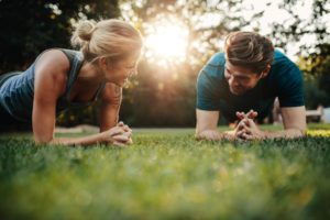 Fit young man and woman exercising in park. Smiling couple doing core workout on grass.