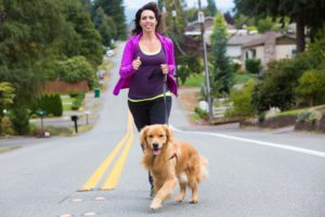A woman jogging up the street with her golden retriever dog.